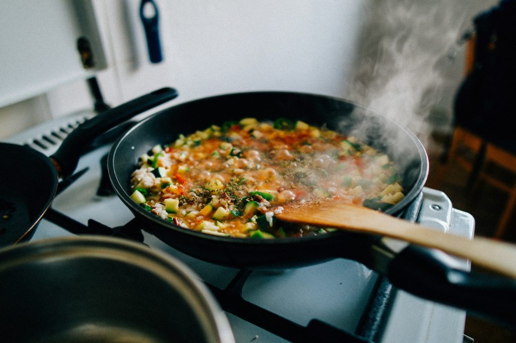 A pan of food on a hob with a wooden spoon. Contextual stock photograph.