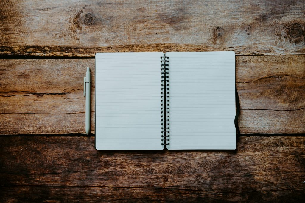 An open blank lined notebook with a pen on a wooden table.